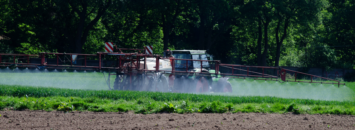 Traktor versprüht Pflanzenschutzmittel auf landwirtschaftlicher Fläche.