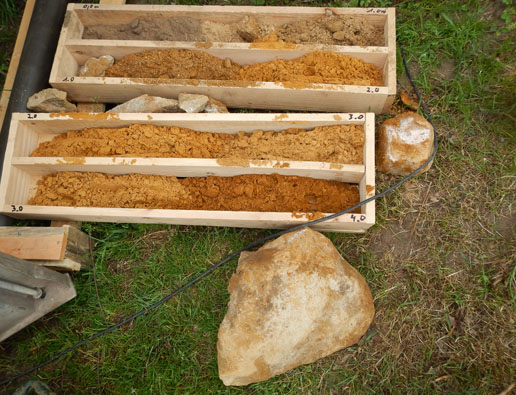 Foto der Kernbohrung bei Reken-Westerhok: sandige Grundmoräne in den Bohrkernkisten sowie daneben liegende Findlinge