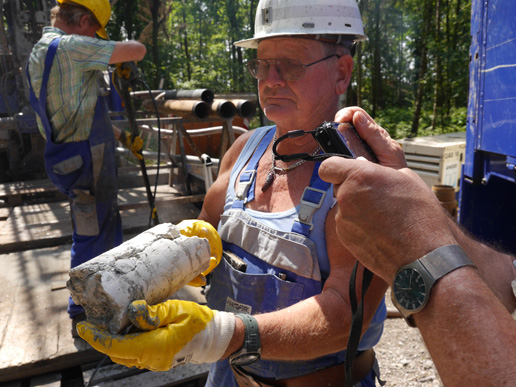 Foto vom Bohrplatz, der Bohrmeister hält ein Stück Bohrkern aus der Oberkreide in der Hand