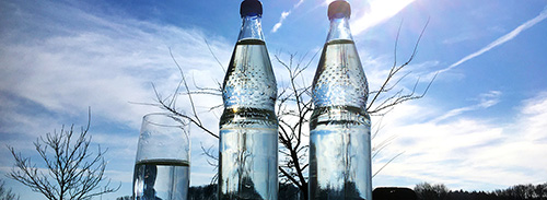 Foto: Mineralwasserflaschen mit Glas vor blauem Himmel